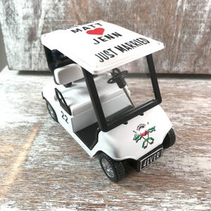 May include: A white toy golf cart with black accents. The cart's roof reads "Matt Jenn Just Married" with a red heart. The front displays a logo and the word "4EVER". The number "22" is on the side.