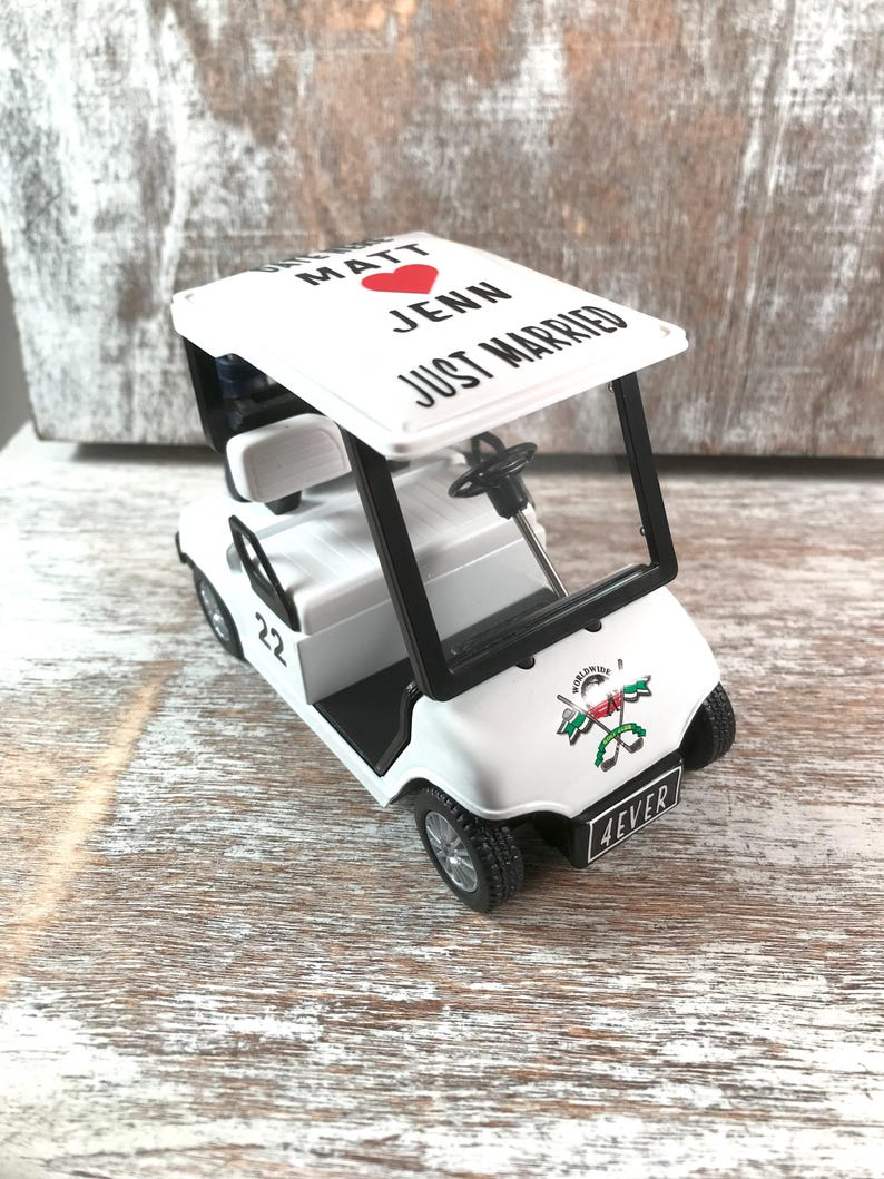 May include: A white toy golf cart with black accents. The cart's roof reads "Matt Jenn Just Married" with a red heart. The front displays a logo and the word "4EVER". The number "22" is on the side.