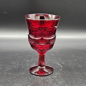 May include: A red glass goblet with a stemmed base. The goblet has a decorative pattern around the rim and body.