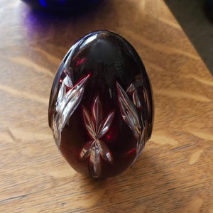 Puede incluir: Un huevo de cristal rojo con un diseño de vidrio cortado. El huevo está sobre una superficie de madera.