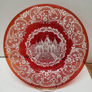 以下が含まれることがあります： 縁に白いレース模様が施された赤いガラスの皿。皿の中央には、ドームのある建物の白い画像が描かれている。