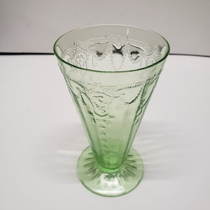 May include: A vintage green glass sundae or dessert glass. The glass has a conical shape with a decorative etched pattern around the rim and on the sides. The base is a circular footed design. The glass is a light green color.