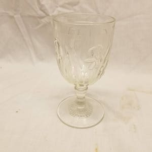 May include: A clear glass goblet with a stemmed base and a decorative pattern. The goblet is made of clear glass and has a delicate, elegant design.