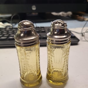 May include: Two vintage glass salt and pepper shakers with silver tops. The shakers are yellow and have a floral pattern.