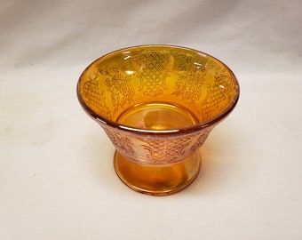 May include: A vintage amber glass bowl with a footed base. The bowl has an intricate floral and geometric design.