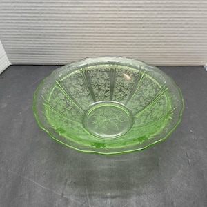 May include: A translucent light green glass bowl featuring a scalloped rim and a pressed floral pattern. The interior of the bowl displays a detailed embossed design of flowers and leaves radiating from the center, with vertical panels.