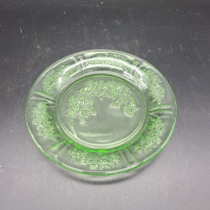 Puede incluir: Un plato de vidrio verde con un diseño floral. El plato tiene un borde elevado y un borde festoneado.