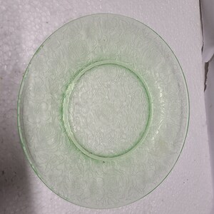 May include: A green glass plate with a floral design. The plate has a raised rim and a centre well.