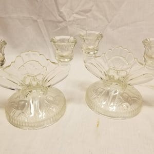 May include: A pair of clear glass candle holders with a floral design. Each holder has three candle cups and a wide base.