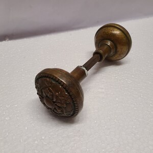 May include: Antique brass door knob with a decorative floral design. The knob is attached to a spindle.