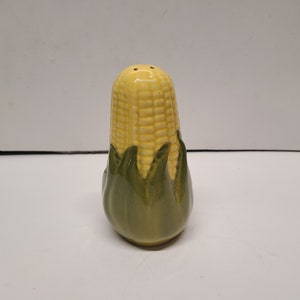 Puede incluir: Un salero y pimentero de cerámica con forma de mazorca de maíz. El maíz es amarillo y la cáscara es verde.