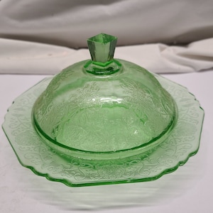 May include: A vintage green glass butter dish with a domed lid and a delicate floral pattern.
