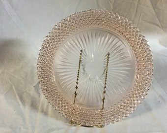 May include: A pink glass serving plate with a diamond pattern around the edge and a sunburst pattern in the center. The plate is on a gold metal stand.