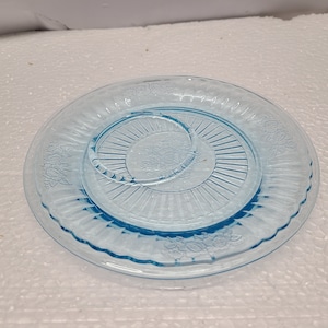 Könnte beinhalten: Ein hellblauer Teller aus Glas mit einem gewellten Rand und einem Blumendesign. Der Teller hat einen erhöhten Mittelteil mit einem Sonnenstrahlenmuster.