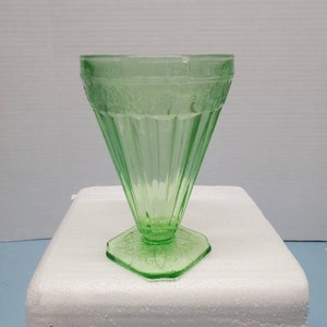 May include: A green glass goblet with a fluted design and a scalloped base. The glass has a vintage look and is perfect for serving drinks.