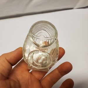 May include: A clear glass jar with a textured surface. The jar has a wide mouth and a rounded bottom.