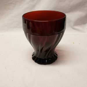 May include: A deep red glass goblet with a swirling design. The goblet has a wide, round bowl and a tall, slender stem.