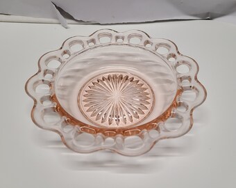 Pode incluir: Uma tigela de vidro rosa com uma borda festonada e um design de vidro cortado. A tigela tem um visual delicado e feminino.
