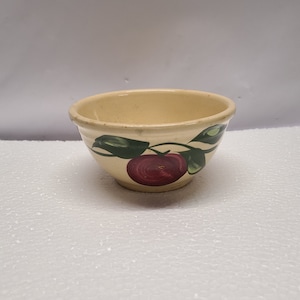 Puede incluir: Un pequeño tazón de cerámica de color crema con un diseño de manzana verde y roja. El tazón es perfecto para servir aperitivos o postres.