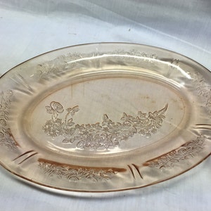 May include: A vintage oval-shaped serving platter made of pink glass with a floral design. The platter has a raised rim and a delicate floral pattern etched into the glass.