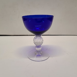 May include: A cobalt blue glass goblet with a clear glass stem and base. The base is textured with a raised pattern resembling a golf ball.