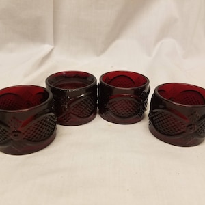 May include: Four red glass napkin rings with a textured design. The rings are made of clear glass with a red tint.