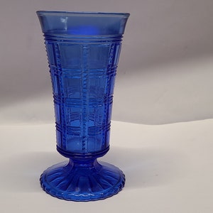 May include: A cobalt blue glass vase with a geometric patterned design. The vase has a flared base and a cylindrical body.