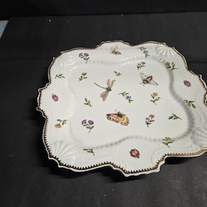 May include: White porcelain serving platter with a scalloped edge and gold trim. The platter is decorated with colorful butterflies, dragonflies, ladybugs, and floral accents. A decorative piece for serving food or displaying as a decorative item.