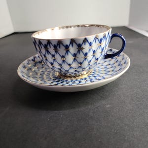 Xícara de chá com pires, em azul cobalto com detalhes em ouro branco, capacidade de 240 ml (8 oz). 5,7 cm de altura por 9,5 cm de diâmetro.