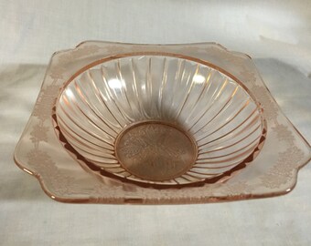 May include: A square, pink glass bowl with a scalloped edge and a delicate floral pattern. The bowl has a fluted interior.