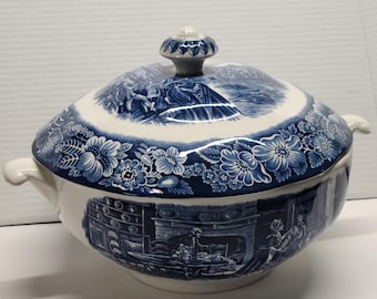 Könnte beinhalten: Eine blau-weiße Keramik-Suppenterrine mit Deckel. Die Terrine hat ein Blumen- und Landschaftsdesign. Sie hat zwei Griffe und einen dekorativen Knopf auf dem Deckel. Das Design ist in einem klassischen blau-weißen Farbschema gehalten.