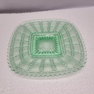 May include: A square green glass dish with a scalloped edge. The dish has a raised, geometric pattern and a smaller square in the centre.