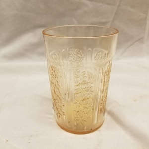 Puede incluir: Un vaso de vidrio transparente con un delicado patrón floral. El vaso tiene un tono rosa pálido y es perfecto para servir bebidas.