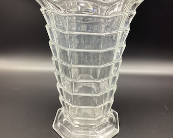 May include: A clear glass vase with a geometric design. The vase has a wide mouth and a narrow base. It is made of thick glass and has a scalloped rim.