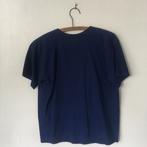 以下が含まれることがあります： 木製のハンガーにかけられた紺色のTシャツ。ハンガーには「Thompson Bros.」の文字が印刷されています。