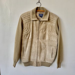 May include: A beige suede jacket with a zipper closure and ribbed knit trim. The jacket has a quilted design on the shoulders and back.