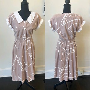 Könnte beinhalten: Ein beiges Midikleid mit weißem Kragen und kurzen Ärmeln. Das Kleid hat ein weißes abstraktes Muster und eine taillierte Passform.