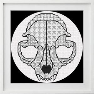 May include: Black and white cross-stitch pattern of an animal skull with geometric designs. The skull is in a circle on a black background.