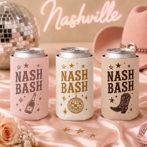 May include: Three cylindrical beverage can coolers in light pink, cream, and beige. Each features the text "NASH BASH" with star accents. The pink cooler shows a champagne bottle, the cream one a disco ball, and the beige one a cowboy boot.