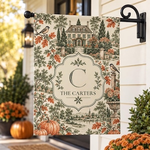 May include: A rectangular garden flag featuring a cream-coloured background with a central ornate frame containing the letter C and the text THE CARTERS. The design includes a detailed landscape with a house, trees, birds, pumpkins, and foliage.