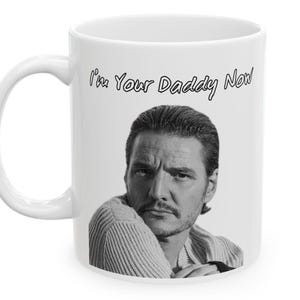 Könnte beinhalten: Weiße Keramiktasse mit einem Schwarz-Weiß-Bild eines Mannes und dem Text "I'm Your Daddy Now". Der Text ist in einer handschriftlichen Schriftart gehalten. Die Tasse hat einen gebogenen Henkel.