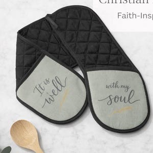 May include: Black quilted oven mitt with gray accents. The mitt features the phrases "It is well" and "with my soul" in script. The text "Christian Kitchen Gift" and "Faith-Inspired Design" are also visible.