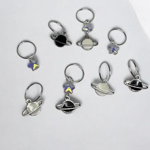 May include: Eight silver hair clips with planet and star charms. The charms are in black, white, and iridescent purple.