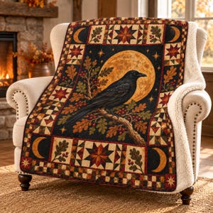 Peut inclure: Un plaid rectangulaire représentant un corbeau noir perché sur une branche de chêne devant une grande lune jaune. La bordure présente un motif de croissants de lune, d'étoiles, de feuilles de chêne et de baies dans des tons noir, or, rouge et marron.