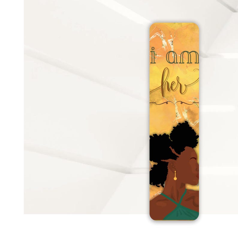 May include: A yellow and gold bookmark with a black and brown illustration of a woman with an afro. The text "i am her" is written in green and brown on the bookmark.