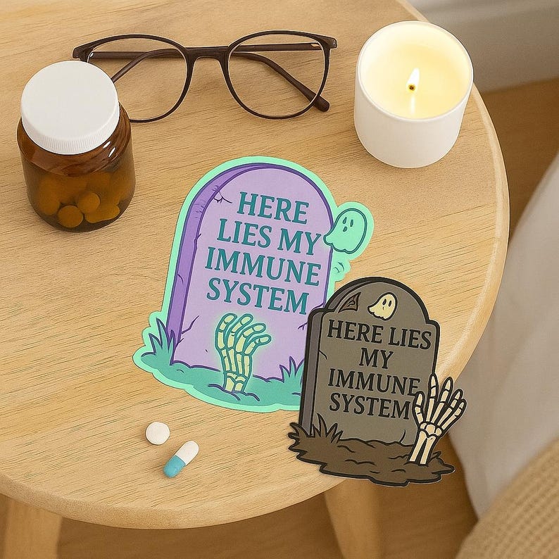 Pastel and dark Here Lies My Immune System stickers flat lay on nightstand with pill bottle, glasses, candle, and medications. Funny spoonie vinyl decals for chronic illness community, relatable gift.