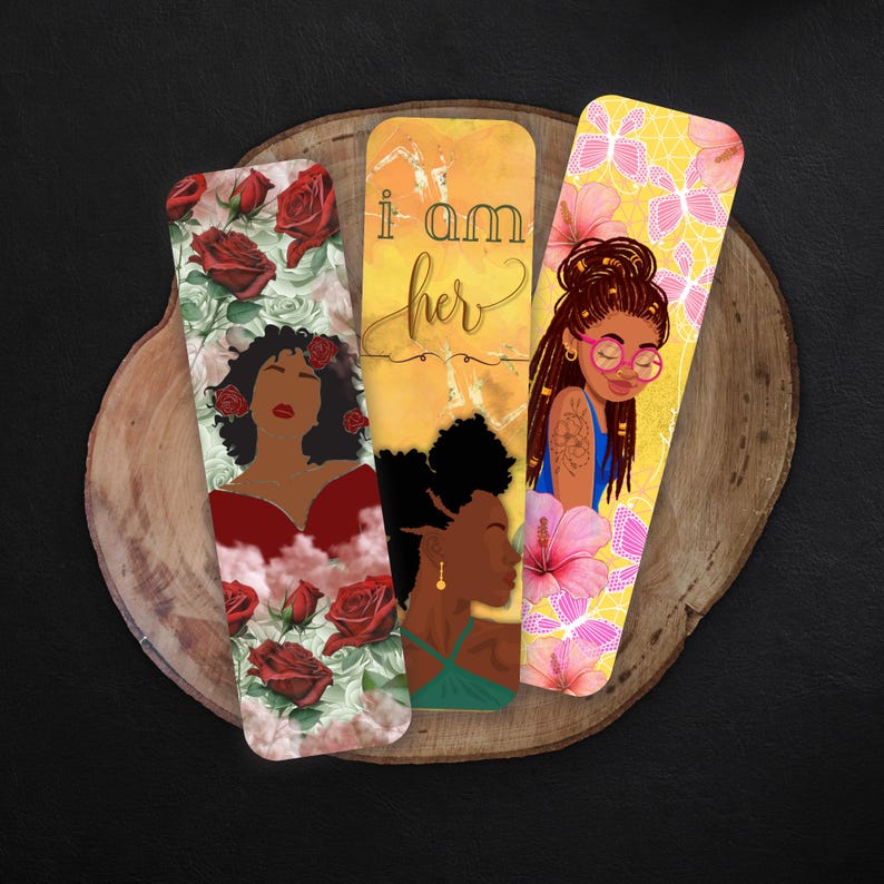 May include: Three bookmarks with different designs. The first bookmark has a red rose floral design with a black woman in a red dress. The second bookmark has a yellow background with the text 'i am her' and a black woman with an afro. The third bookmark has a yellow background with pink flowers and butterflies and a black woman with long braids and glasses.