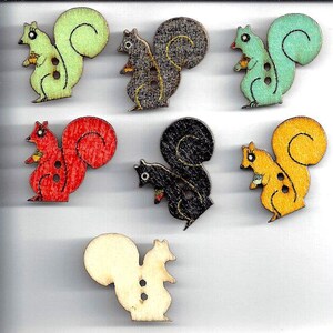 May include: Six wooden squirrel buttons in various colors, including green, gray, blue, red, black, and yellow. The buttons are approximately 1 inch in diameter and have two holes for sewing. The buttons are arranged in two rows of three, with a ruler below them.