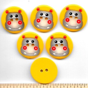 May include: A collection of yellow buttons with a hippo face design. The buttons have a yellow background with a gray hippo face, red cheeks, and black eyes. One button is plain yellow with two holes.