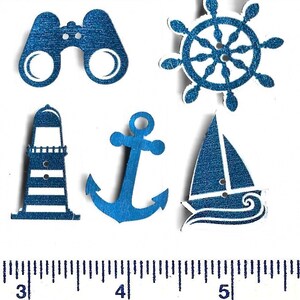 May include: A selection of nautical-themed wooden buttons in blue and white. The set features binoculars, a ship's wheel, a lighthouse, an anchor, and a sailboat. The image also shows a ruler with centimetre measurements.